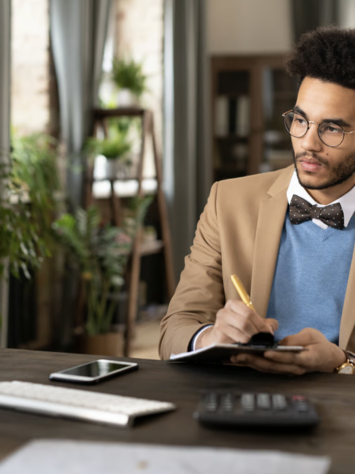 Accountant making notes on a clipboard at his desk, calculator and papers in front of him